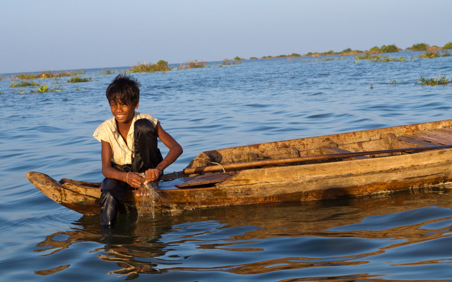 Young boy fishing in Tonle Sap at sunset.